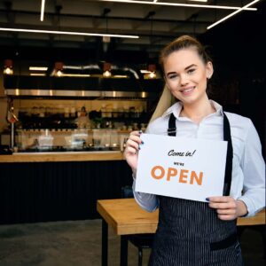 Young small business owner holding a sign that reads “Come in! We’re open!”